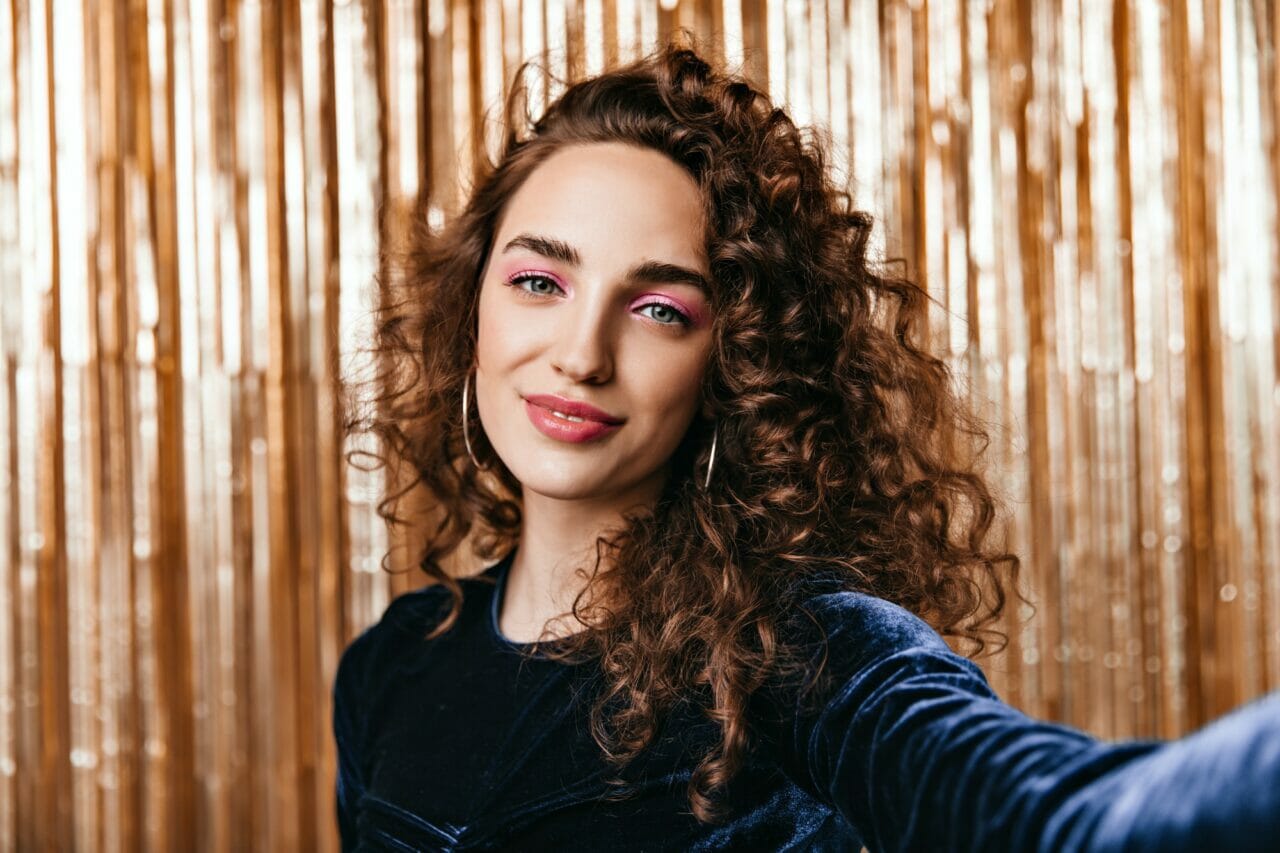 curly lady in good mood taking selfie on gold background