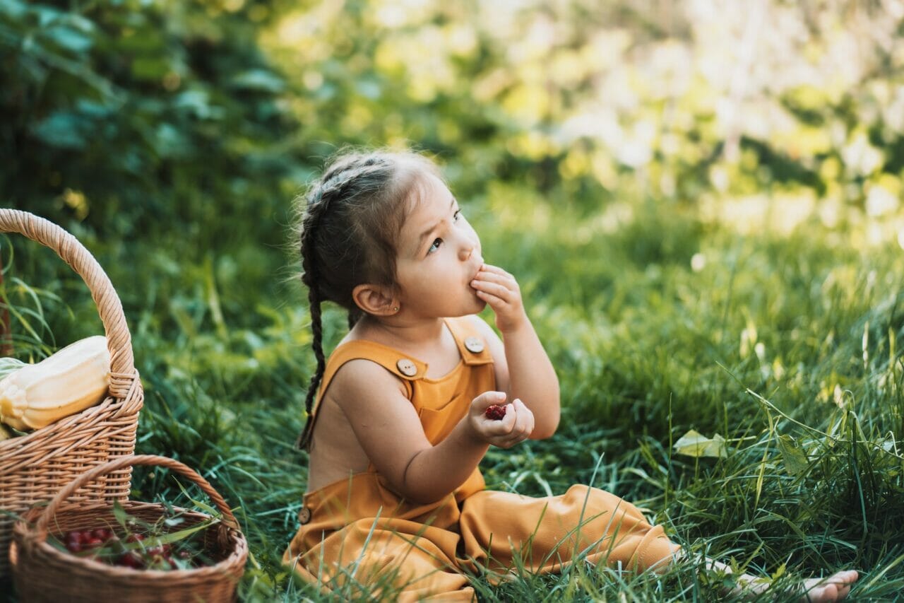 girl in overalls sitting on the grass and eating raspberries