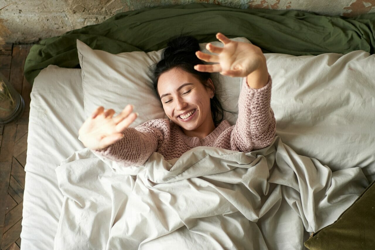 young brunette woman stretching at home on bed after sleep