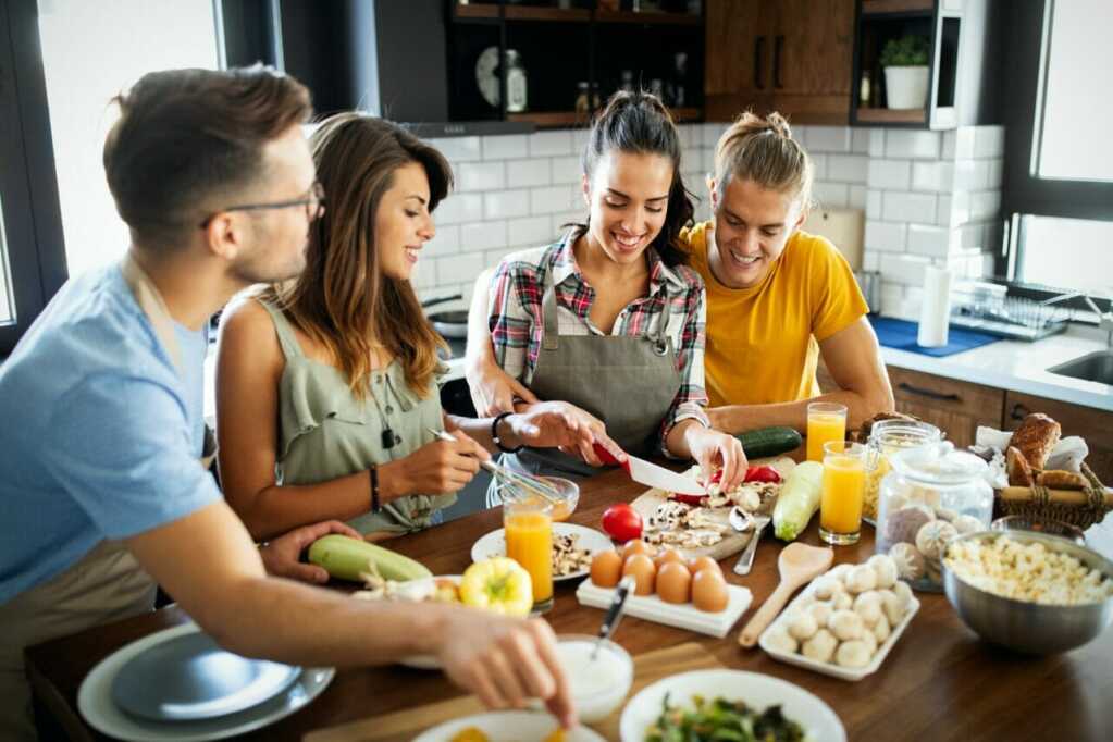 Group of happy friends laughing and talking while preparing meals in kitchen